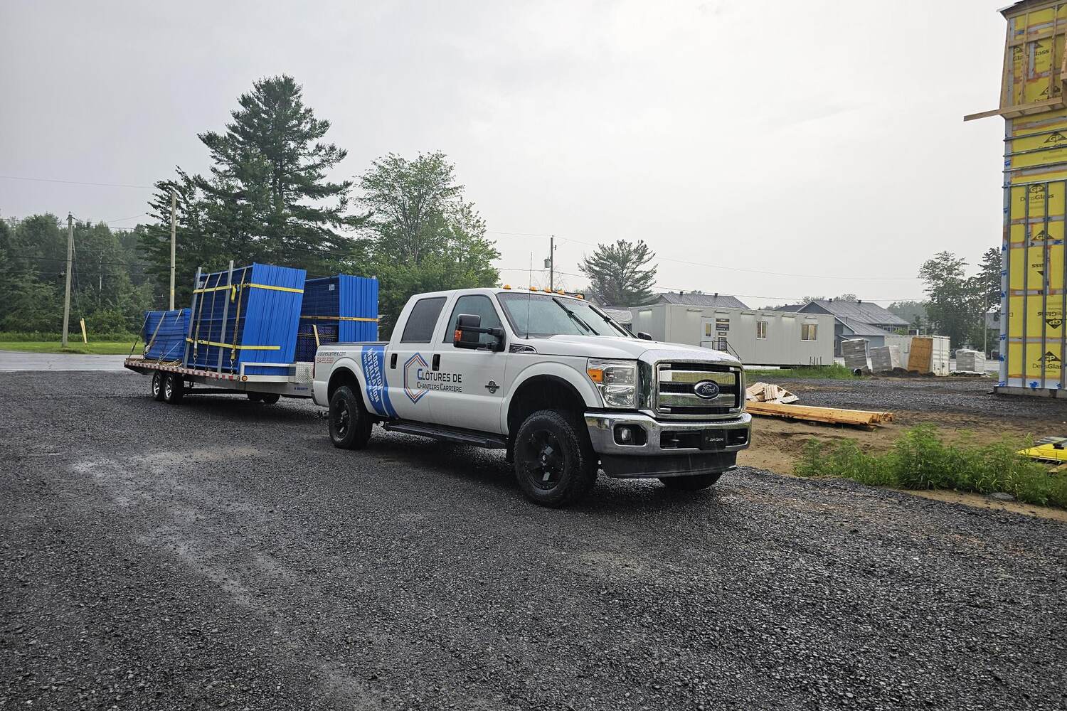 Camionnette blanche de Clôtures de chantier Carrière tirant une remorque chargée de panneaux de clôture bleus