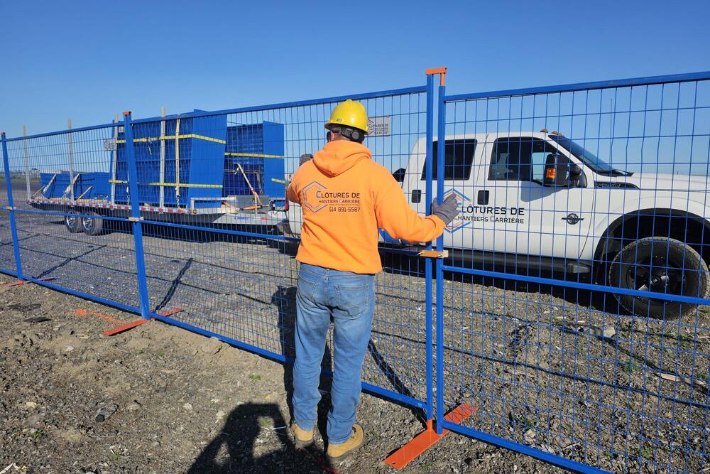 Travailleur de Clôtures de chantier Carrière installant des panneaux de clôture bleus devant une camionnette blanche
